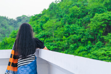 Young woman standing alone on a rooftop looking at the beautiful green mountains nature view. Tranquility, freedom, nature, vacation, and adventure concept.
