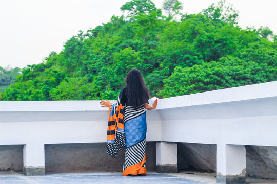 Young woman standing alone on a rooftop looking at the beautiful green mountains nature view. Tranquility, freedom, nature, vacation, and adventure concept. - Powered by Adobe