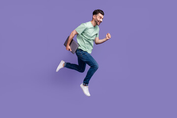 Fototapeta na wymiar Full body photo of attractive young guy run fast hold netbook hurry meeting wear trendy gray outfit isolated on violet color background