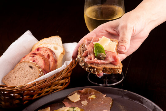 romantic dinner with carpaccio cold meat cattail basket of artisan breads glass of white wine female hand showing a canap&eacute; with caper