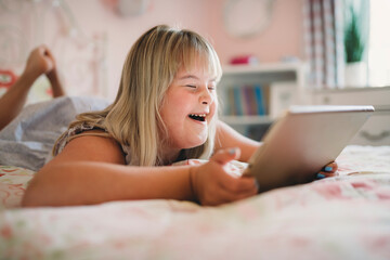 Beautiful little child girl in a dress having great time on her pink bedroom with tablet