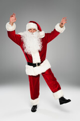 Full length of santa claus in costume dancing on grey background.