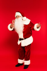 Fototapeta na wymiar Full length of santa claus looking at glass of champagne on red background.