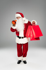 Santa claus in costume and eyeglasses holding loudspeaker and shopping bags on grey background.