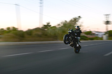 Motorbike rider doing wheelie on the road in the evening.