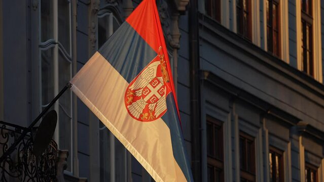 4K video with the national flag of Serbia winding on the balcony of a building during an autumn sunrise. Serbian flag concept video.