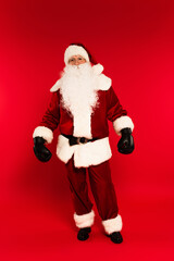 Full length of santa claus in costume and boxing gloves standing on red background.