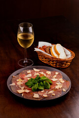 romantic dinner with carpaccio cold meats basket of artisan breads basil leaves mustard dijon glass of white wine wooden table in an angle portrait