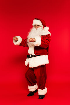 Bearded santa claus looking at camera while dancing on red background.