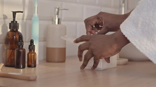 Slowmo closeup of unrecognizable Black woman applying clarifying lotion on cotton pad in bathroom while taking off her makeup and doing skincare routine