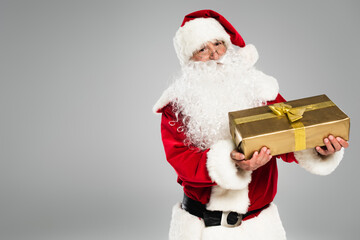 Father christmas in eyeglasses holding gift box with bow isolated on grey.