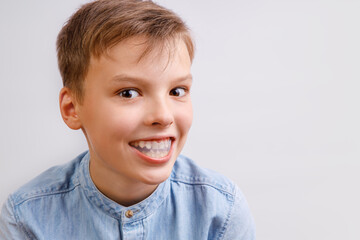 Fototapeta premium Boy is wearing orthodontic silicone trainer or night-guard case. Invisible braces helps of orthodontics problem. Close-up portrait. Mobile appliance for dental teeth correction.