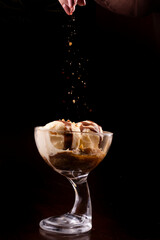 dessert of vanilla ice cream cup with brownie and hot chocolate sauce with chef preparing spreading sweet farofa on top