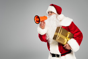 Santa claus in eyeglasses holding loudspeaker and present isolated on grey.