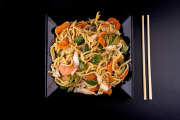 chinese food delivery vegetarian yakisoba black plate viewed from above black background with chopsticks