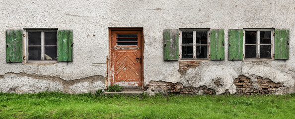 Fototapeta na wymiar Panoramic photo of an old building exterior. Dirty door and windows on damaged wall. Travel, architecture concept