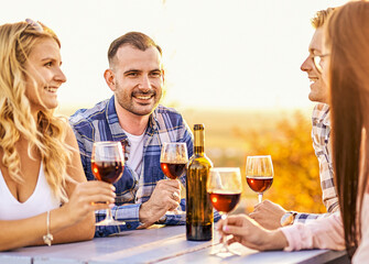 Young friends having fun outdoors - Happy people enjoying harvest time together at farmhouse winery countryside - Youth and friendship concept - Tasting red wine at vineyard before sunset