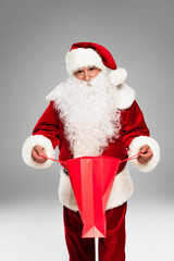 Santa claus in hat opening shopping bag and looking at camera isolated on grey.