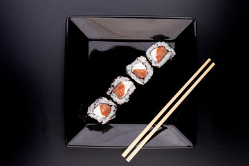 japanese food on black plate with four salmon sushi and cream cheese with soy sauce and chopsticks in top view