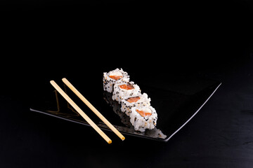 japanese food on black plate with four salmon sushi and cream cheese and chopsticks in angle view