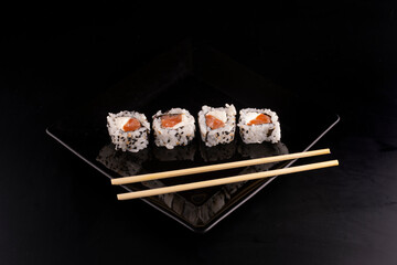 japanese food on black plate with four side by side salmon sushi and cream cheese and chopsticks in angle view