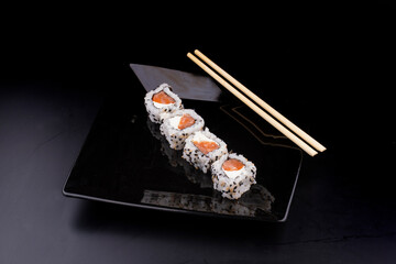 japanese food on black plate with four salmon sushi and cream cheese and chopsticks in angle view