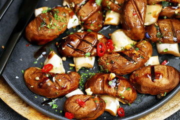 Appetizing juicy grilled mushrooms on a dark plate with spices. Macro.