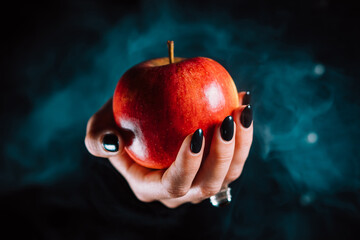 Woman as witch offers red apple - symbol of toxic proposal, lure. Fairytale, white snow, wizard concept. Halloween celebration, cosplay. Smoke, mist background. - obrazy, fototapety, plakaty
