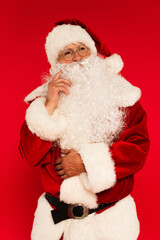 Pensive santa claus in costume looking away isolated on red.
