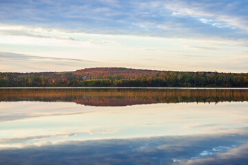 Fototapeta premium Hillside with trees in autumn color reflecting in a calm lake in northern Minnesota