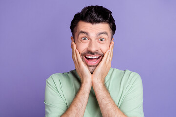 Portrait of crazy impressed positive man with brunet hairdo dressed t-shirt hands on cheekbones isolated on purple color background