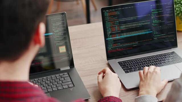Two hipster coworkers sharing ideas about project sitting with laptops in spacious open space office. Developers discuss application program code. Coder and manager consulting software architecture.