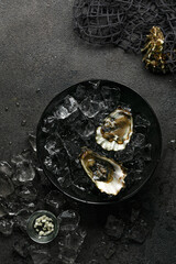 Obraz na płótnie Canvas Fresh opened oysters in a plate with ice on black textured background, top view. Vertical