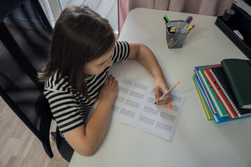 A schoolgirl girl does her homework (writes in a notebook) at home. The concept of back to school. . High quality photo