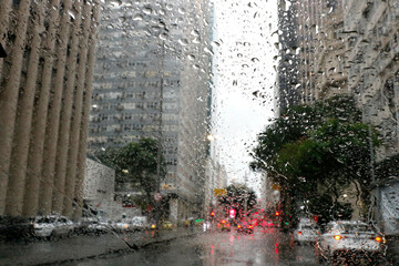 Rain drops on car window. Cold weather rainy season, cloudy wet day. Lonely mood. Town blurry background. Driver point of view.