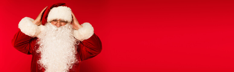 Bearded santa claus in eyeglasses touching head on red background with copy space, banner.