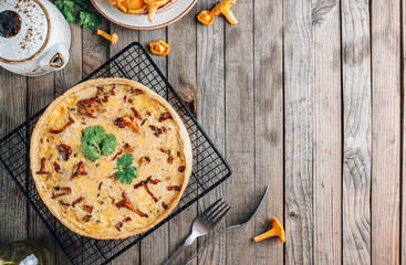 Homemade quiche or tart with chanterelles on rustic wooden background.