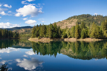 On a sunny Autumn day in Northwest Idaho, the sky and mountainous landscape is reflected in the glassy surface of a peaceful river.