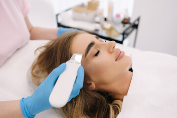 Young woman taking beauty procedure in spa salon. Beautician using peeling device, ultrasonic clining. Gorgeous woman
