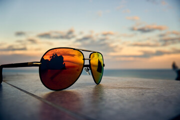 Fototapeta na wymiar Sunglasses at sunny summer day near the sea.Summer vibes. Sunglasses with orange lenses at sunset