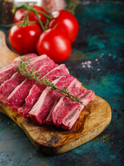 On a wooden cutting board, pieces of raw meat with a sprig of rosemary, appetizing ripe tomatoes on a turquoise marble background. Recipes for cooking homemade steaks.