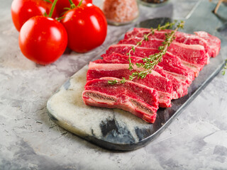 Close-up. Meat raw steaks with a sprig of rosemary on a cutting board, ripe tomatoes and spices on a light background. Restaurant and home cooking recipes, organic food.