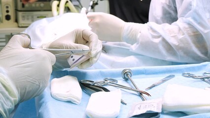 Close-up in surgery, the doctor's hands in sterile gloves take a needle and thread for suturing the wound. The operation is completed and the nurse prepares a needle holder with a needle and thread.