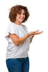 Beautiful middle ager senior woman wearing white t-shirt over isolated background Pointing to the side with hand and open palm, presenting ad smiling happy and confident