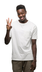 Naklejka premium Young african american man wearing white t-shirt showing and pointing up with fingers number three while smiling confident and happy.