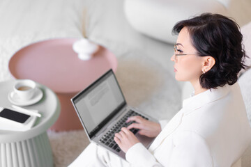 Serious thoughtful middle-aged woman is typing text on a laptop while sitting on the couch. Distant work.