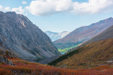 Colorful alpine landscape with small lake among fading autumn colors. Picturesque mountain scenery with motley autumn flora in hanging valley among large mountains. Alpine lake and mountain vastness.