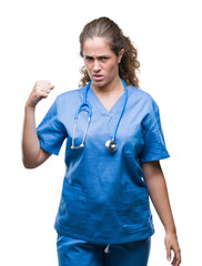 Young brunette doctor girl wearing nurse or surgeon uniform over isolated background angry and mad raising fist frustrated and furious while shouting with anger. Rage and aggressive concept.