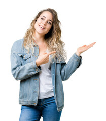 Beautiful young blonde woman wearing denim jacket over isolated background amazed and smiling to the camera while presenting with hand and pointing with finger.