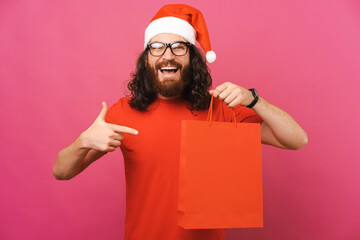 Excited man with Christmas hat is pointing at the shopping bag he holds.
